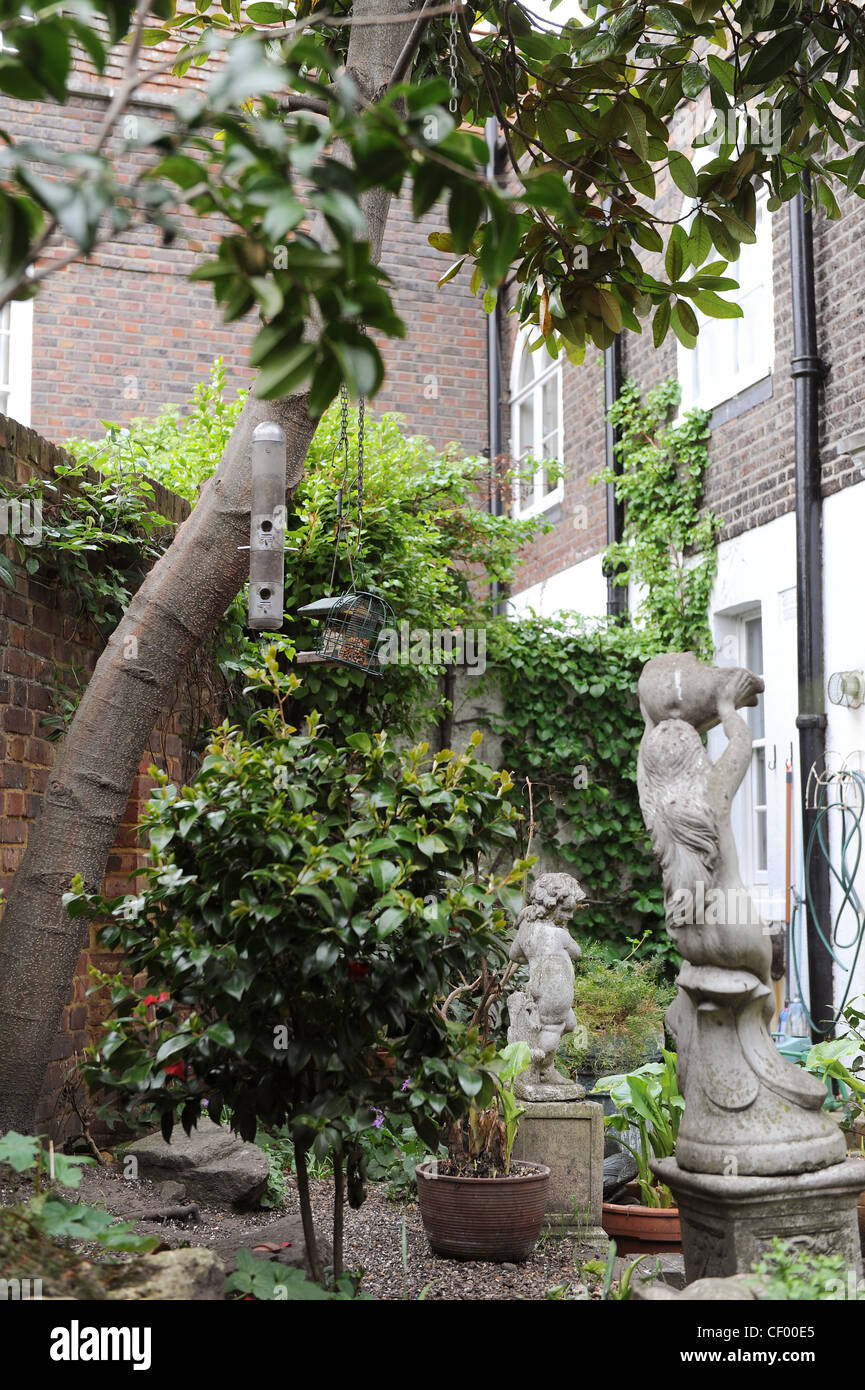 Verborgene Schatz Statuen, Topfpflanzen, Camelia Busch und Futterhäuschen auf dem Baum in der ummauerten Garten hinter dem Haus Stockfoto