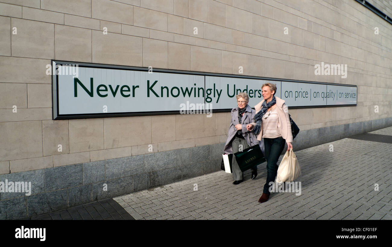 Weibliche Käufer mit Tragetaschen vorbei gehen die John Lewis store Slogan nie bewusst unterboten in Cardiff Wales UK KATHY DEWITT Stockfoto