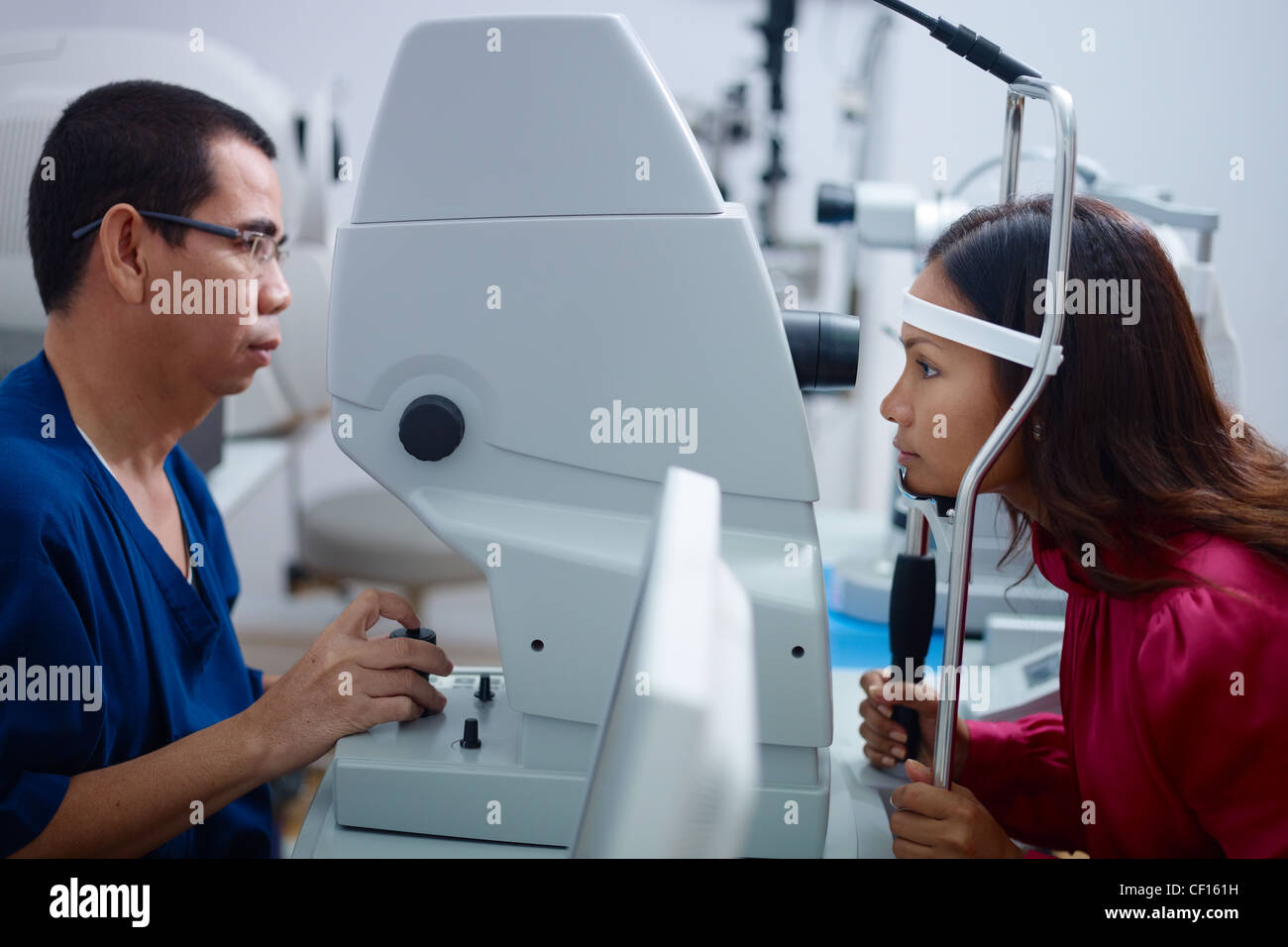 Asiatischen Arzt bei der Arbeit während der Sehkraft Examen zur erwachsenen Frau im Krankenhaus. Seitenansicht Stockfoto
