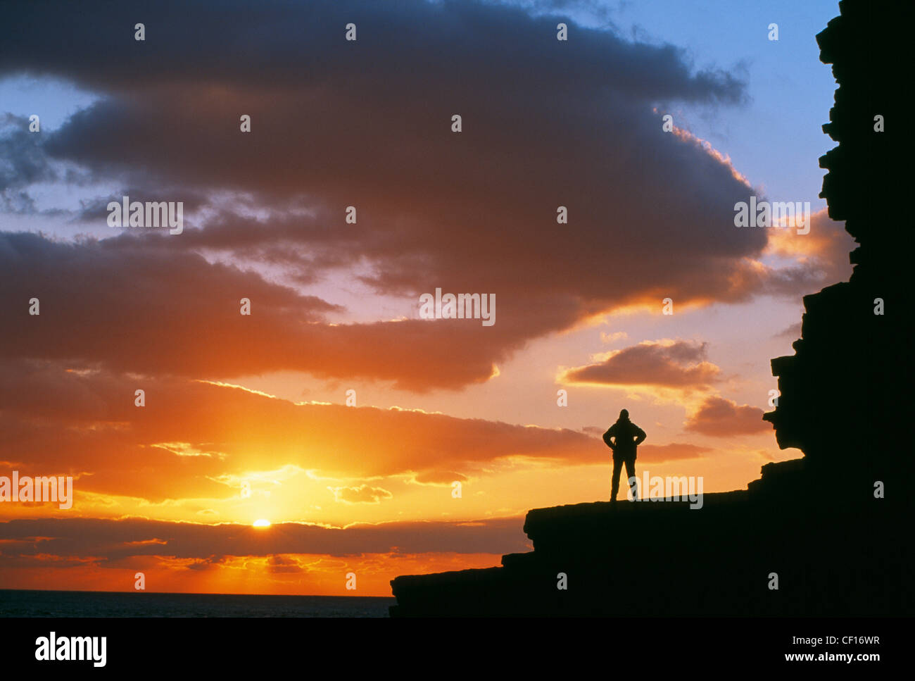 Eine einsame Gestalt steht thront auf oben auf einer Klippe am Nash Punkt Silhoutted bei Sonnenuntergang. Stockfoto