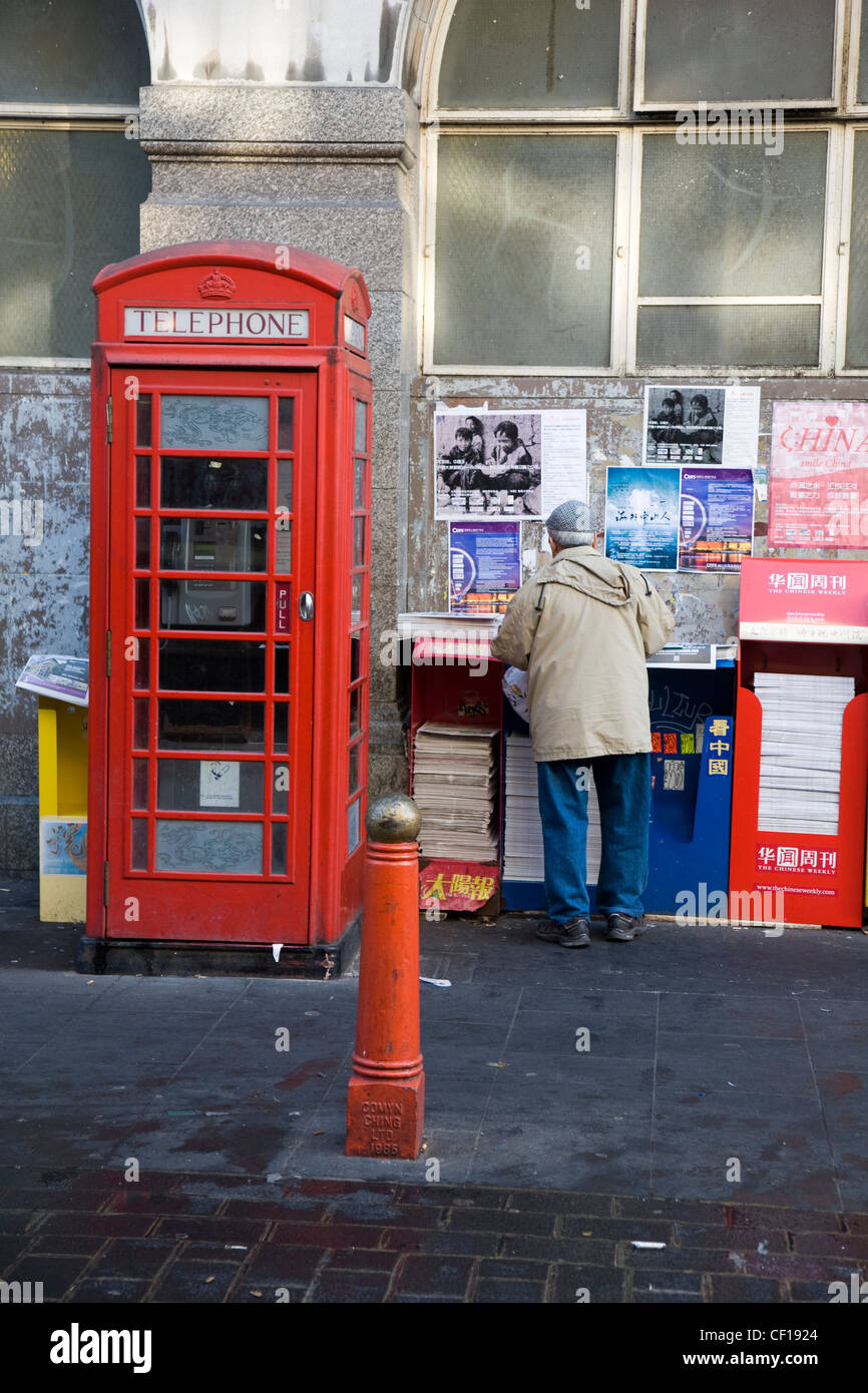 Menschen sammeln und lesen kostenlose chinesische Zeitungen aus einem Zeitungskiosk in Chinatown, London Stockfoto