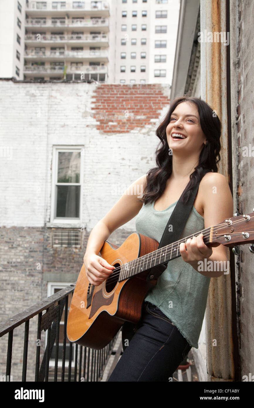 Frau spielt Gitarre auf Feuerleiter Stockfoto