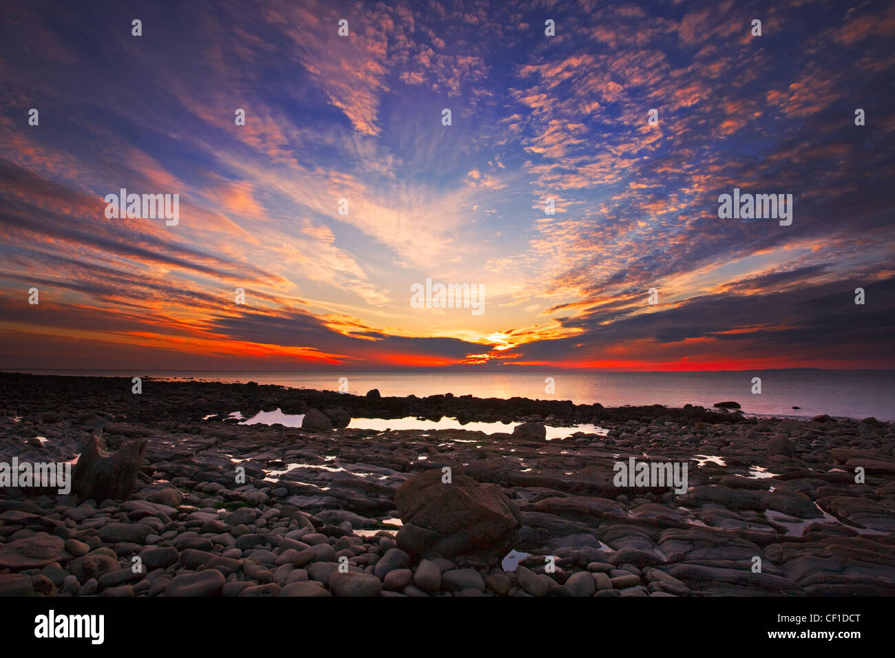 Blick über Felsen und Kieselsteine am Strand in der Nähe von Llwyngwril auf einen wunderschönen Sonnenuntergang nach einem Gewitter. Stockfoto