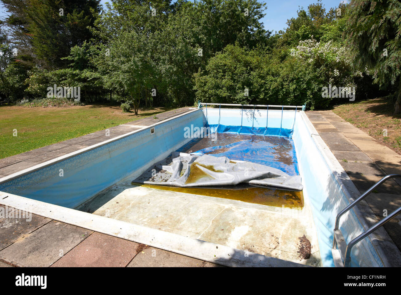 Eine leere, unordentlich, privaten Swimmingpool in einem Garten, umgeben von Sträuchern. Stockfoto