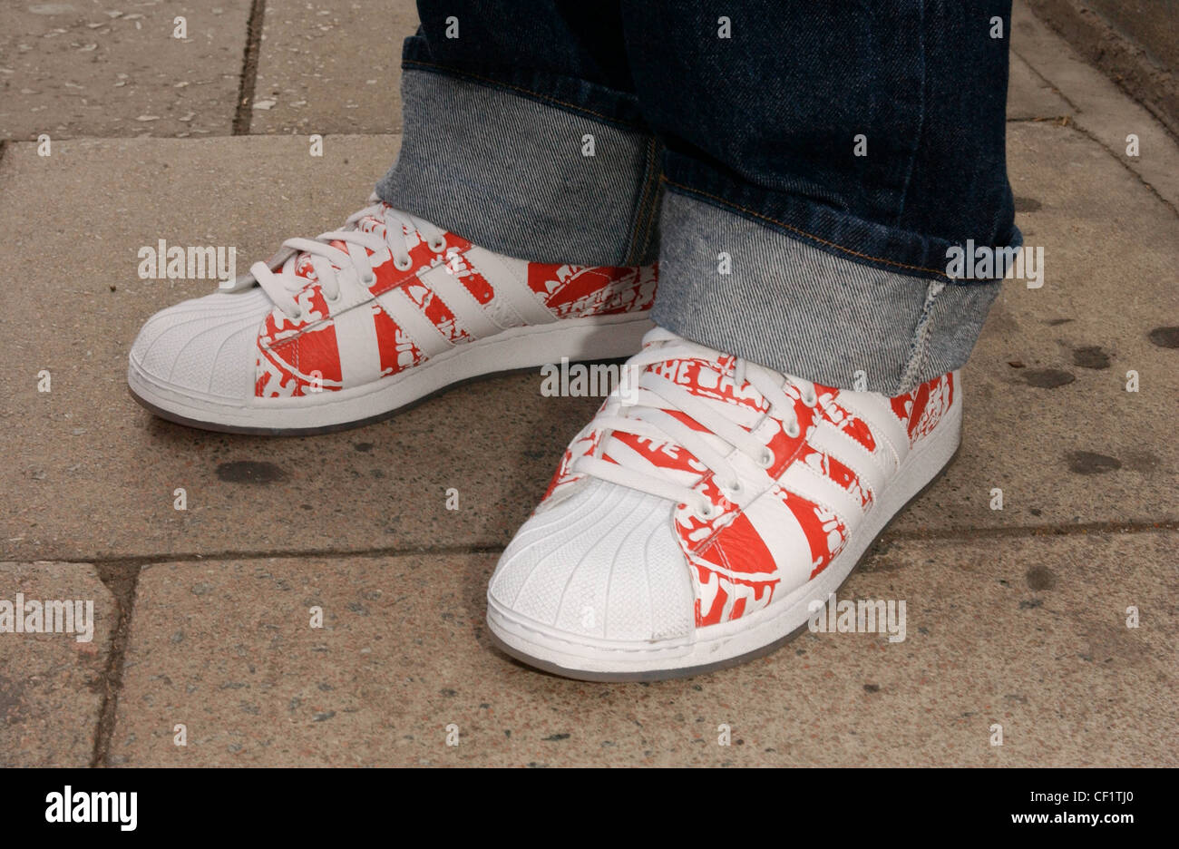 London Street Fashion beschnitten männliche Füße trägt blaue Jeans mit Turn-Ups und rot-weiß-Trainer von Adidas Stockfoto
