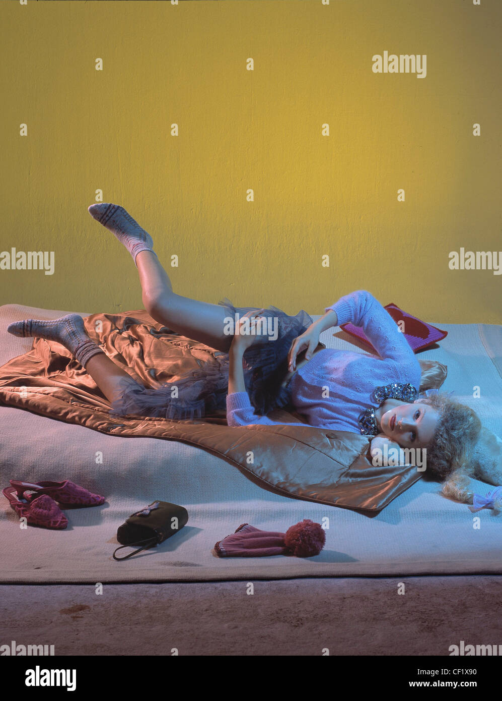 Weibliche blonde Locken aus Gesicht geflochten tragen rosa Strickjacke Sequinned Halsband Spitze und Net Rock Beige gemusterte Socken liegen Stockfoto