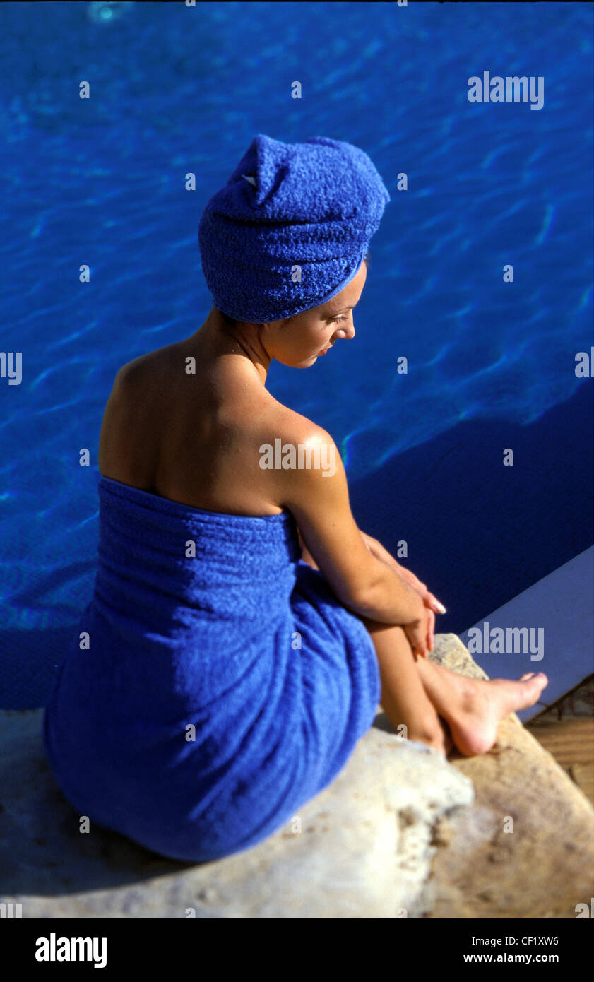 Rückansicht des weiblichen blaues Handtuch umwickelt Körper und Haar, eingehüllt in blaue Handtuch sitzen auf Steinhaufen Hände auf Knien Stockfoto