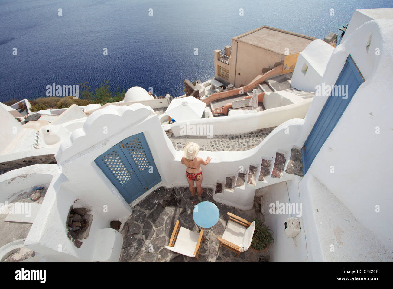 Eine Luftaufnahme von einem traditionellen Höhle Haus im Dorf Oia mit einer Dame, genießen den Blick auf die Caldera und das Meer Stockfoto