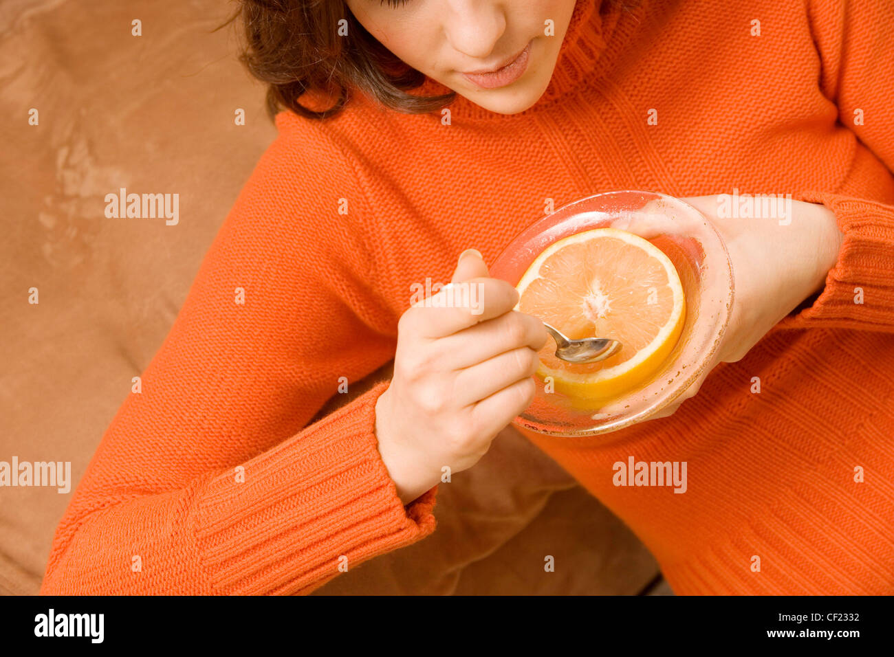 Weibliche Schulter brünette Haare trägt eine orange Überschlag Hals Pullover hält eine Schüssel, eine halbe Grapefruit und Löffel Stockfoto