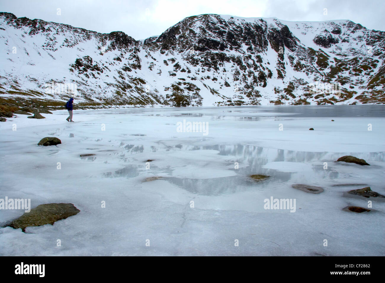 Ein Wanderer erkunden die Eis bedeckt weite des Red Tarn unter dem Schnee begrenzt Gipfel des Lakelandpoeten. Stockfoto