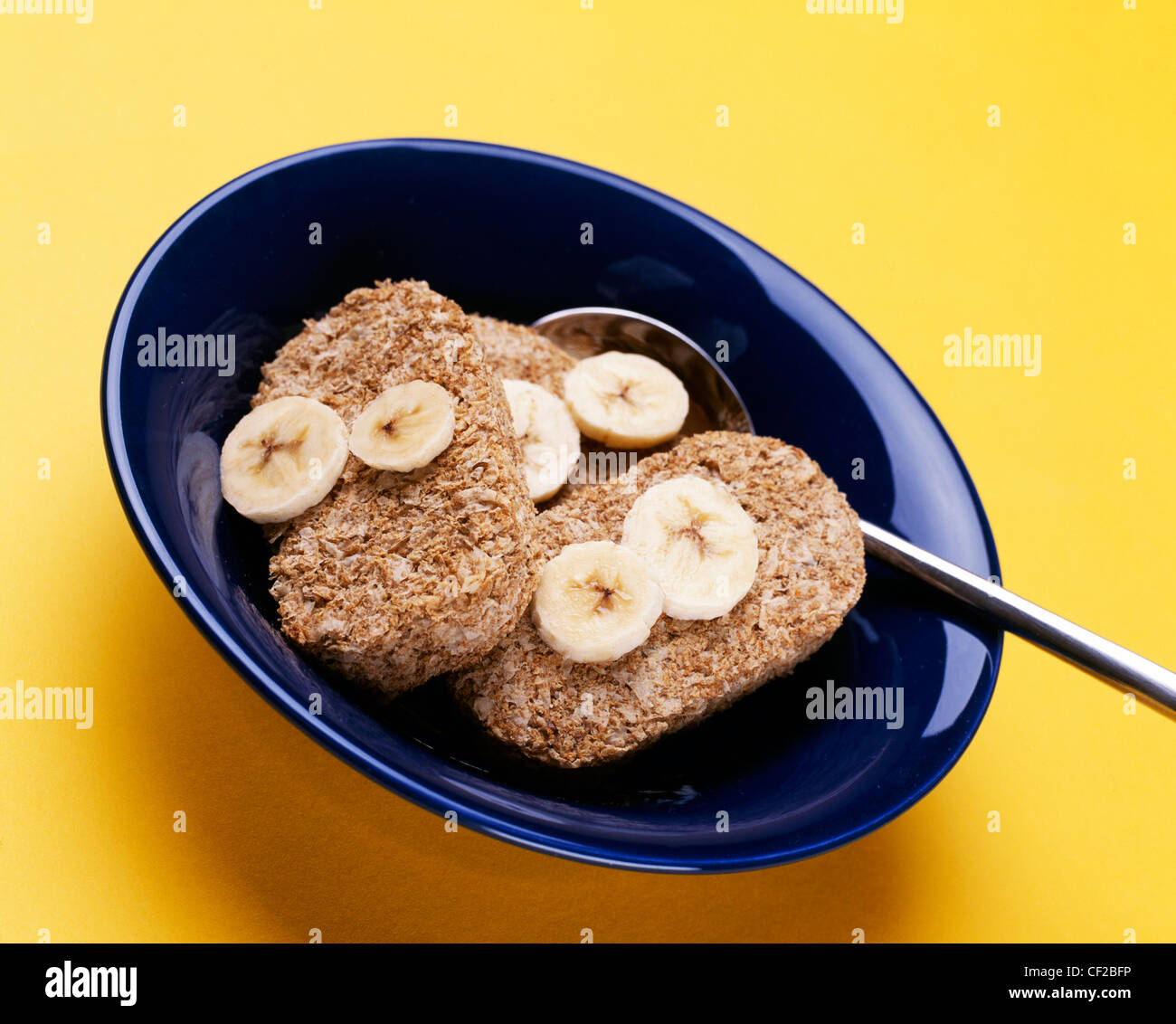 Drei Weetabix Bars mit in Scheiben geschnittenen Bananen in eine blaue Schale mit Löffel Stockfoto