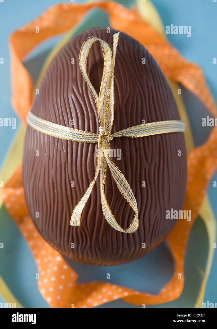 Schokoladen-Osterei mit Goldband mit Orangen und gelben Bändern um ihn herum gebunden Stockfoto