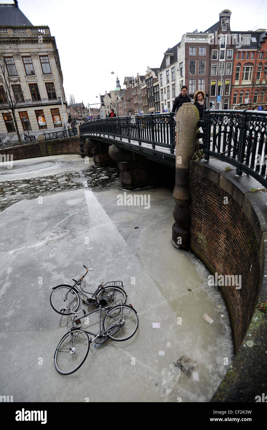 Zwei Fahrräder liegen auf dem Eis eines zugefrorenen Kanals in Amsterdam, Niederlande. Stockfoto