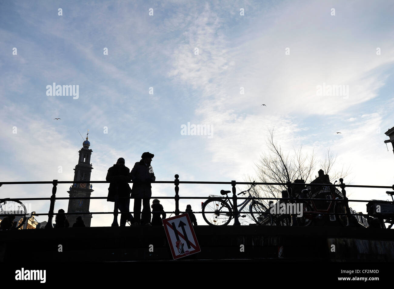 Zwei Menschen Silhouette gegen den Himmel, während er auf eine Kanalbrücke vor der Westerkerk in Amsterdam, Niederlande. Stockfoto