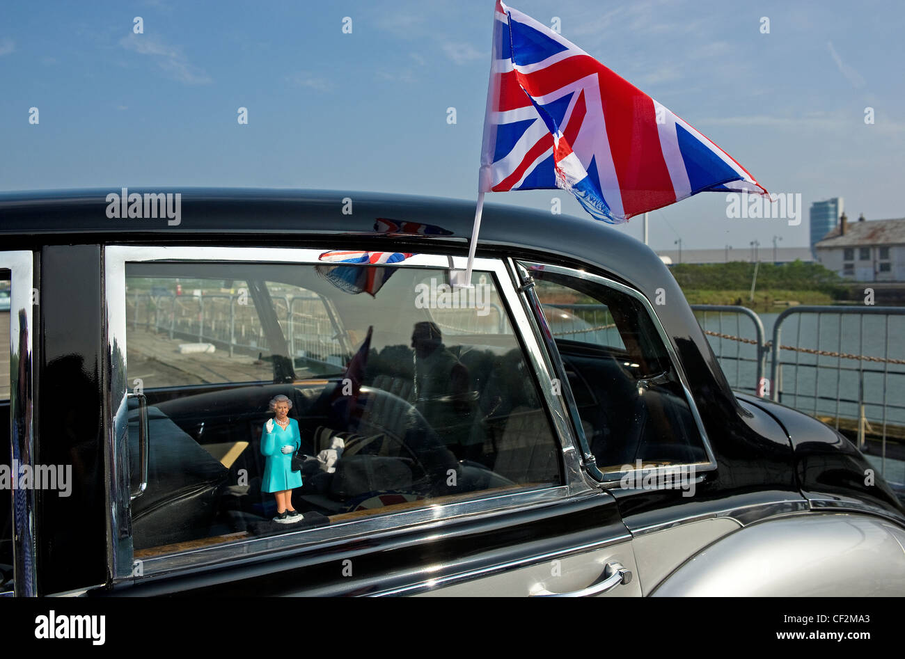 Eine kleine Figur der Königin Elizabeth ll im Fenster einen Oldtimer und ein Anschluß-Markierungsfahne an der Außenseite befestigt. Stockfoto