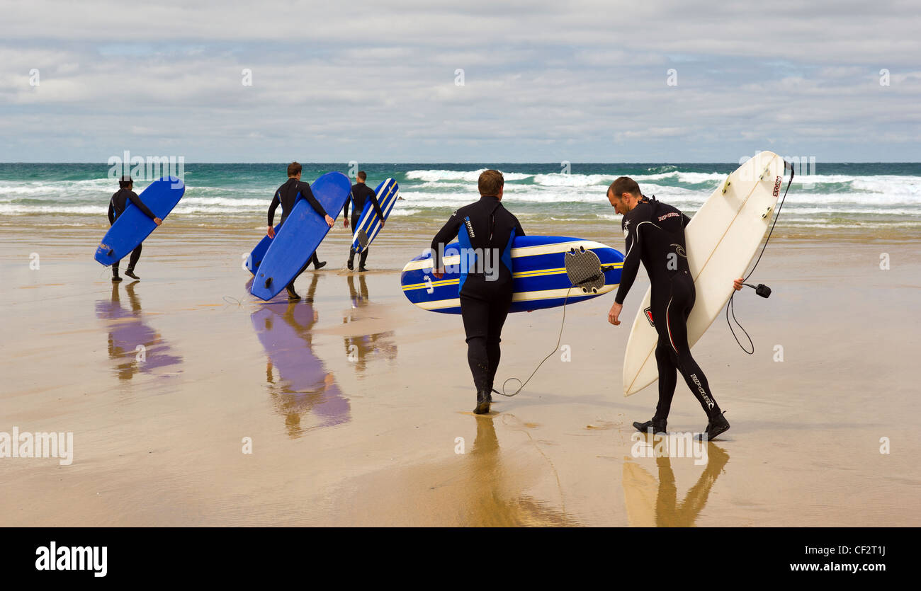 Eine Gruppe von Surfern mit ihren Surfbrettern, die ihren Weg über Fistral Strand heraus zum Meer. Stockfoto