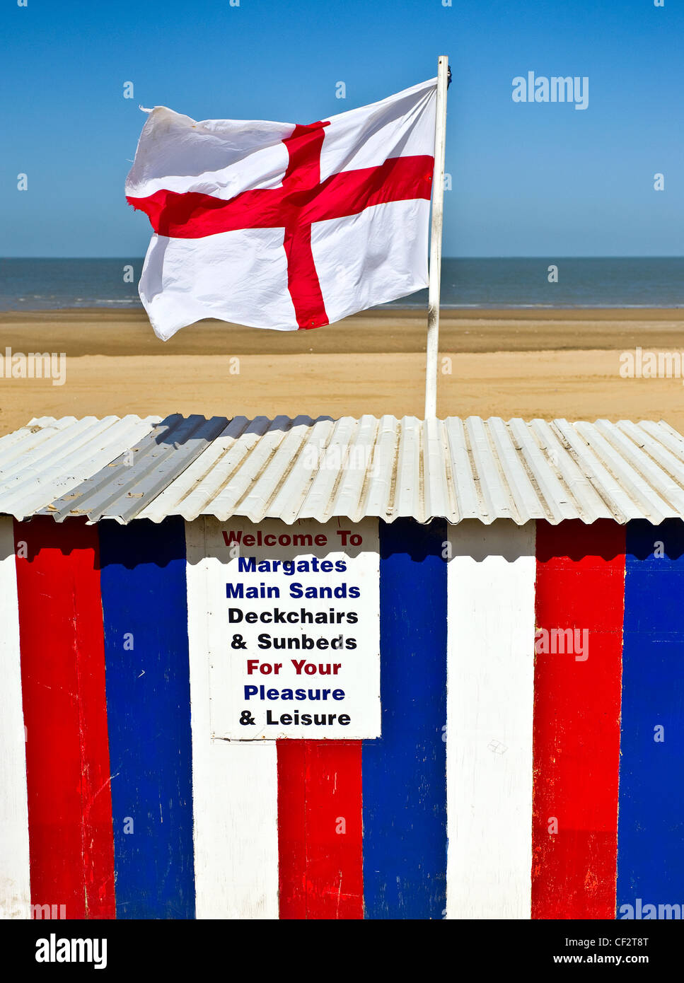Eine englische Flagge, das Kreuz von St. George, fliegen über eine gestreifte Hütte bietet Liegestühle und Sonnenliegen auf Margate Main Sands. Stockfoto