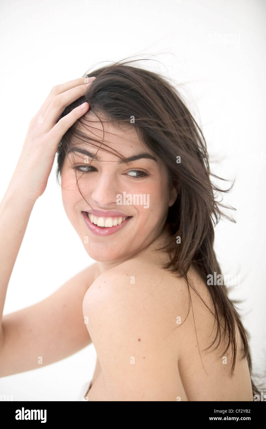 Weibliche lange brünette Haare weht und weißen Tuch umwickelt Brust, rückblickend über die Schulter zu Seite Lächeln, gegen Stockfoto