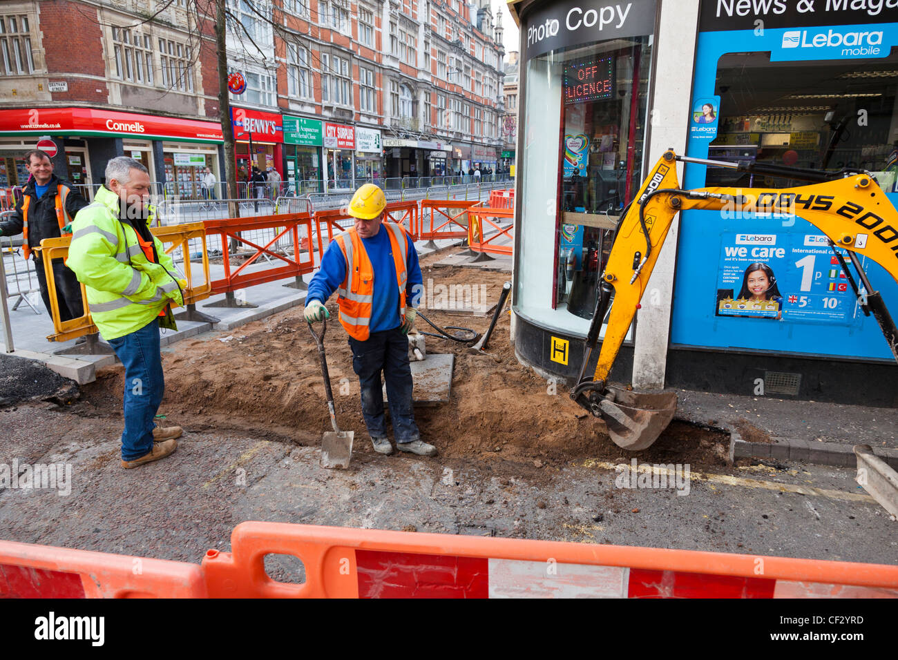 Auftragnehmer einen Graben in der Straße und Gehweg mit einem mechanischen Bagger, Leicester, England. Stockfoto