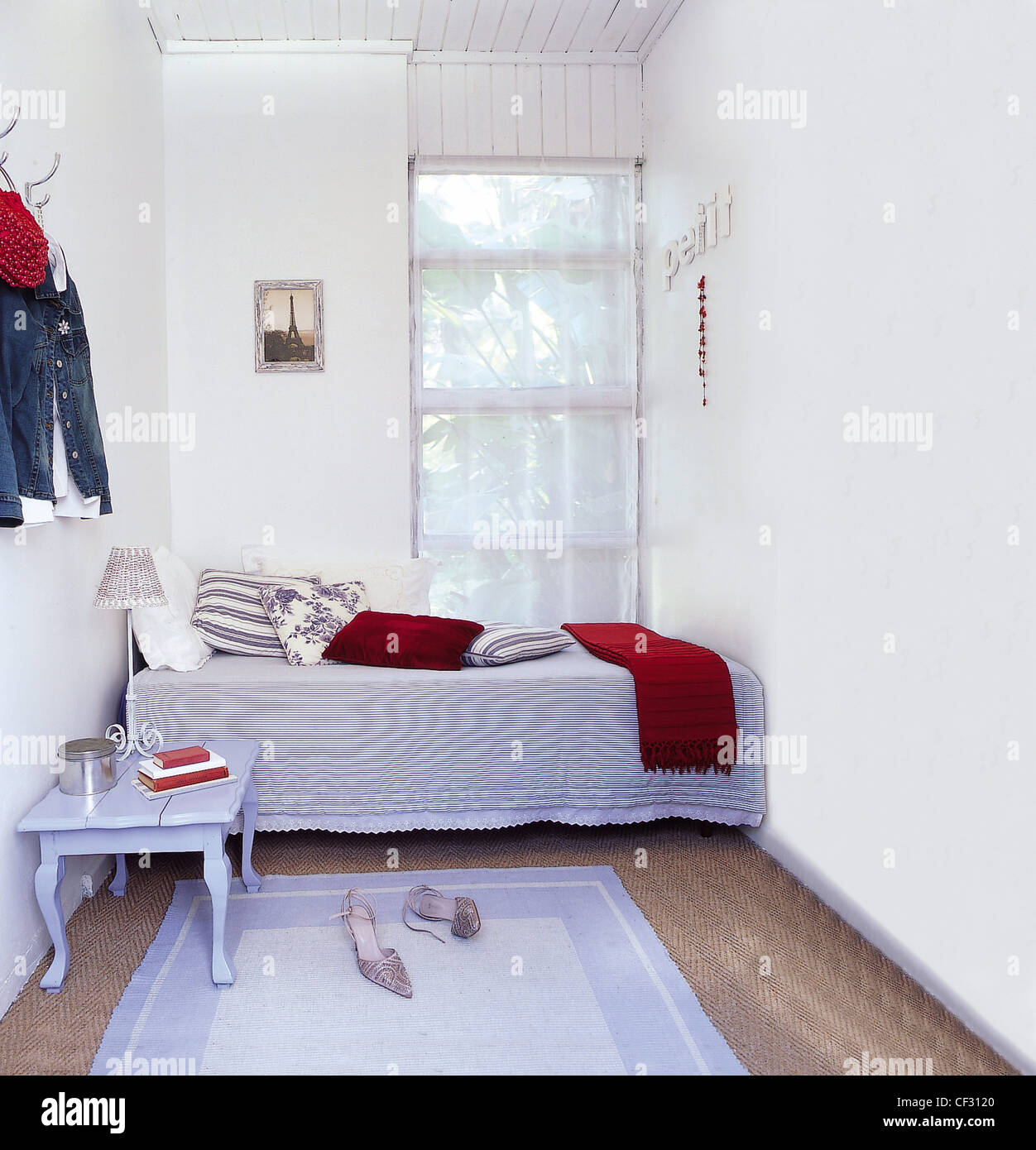 Französischer Flair kleine weiße Schlafzimmer Einzelbett am anderen Ende durch Fenster sortiert gemusterte Kissen auf wenige gestreift blau lackiert Stockfoto