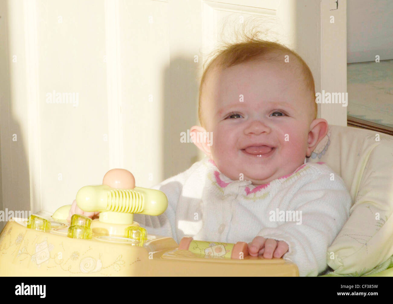 Weibliches Baby, Monate alt war, trug ein weißes Top, sitzt im Lauflerngerät, lächelnd, Blick nach oben Stockfoto