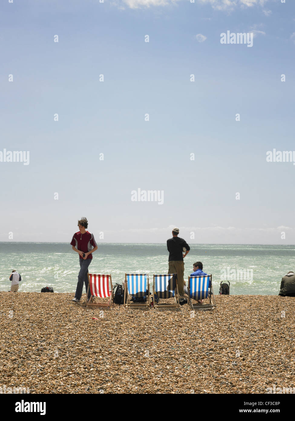 Liegestühle und Menschen auf Brighton Strand an einem sonnigen Tag mit blauem Himmel. Stockfoto