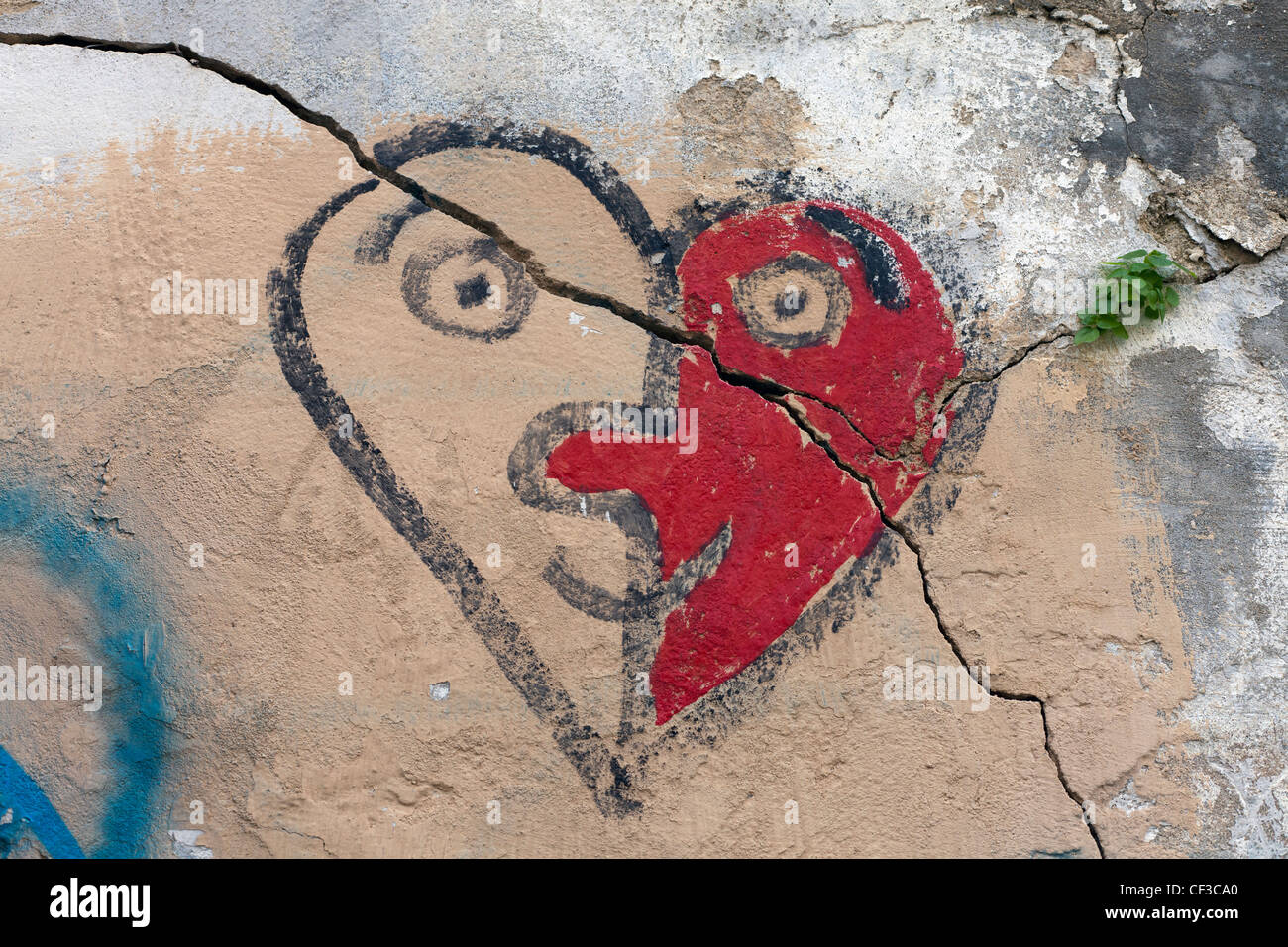 ein Riss durch einen gemalten Herzen ähnelt ein Gesicht an der Wand Stockfoto