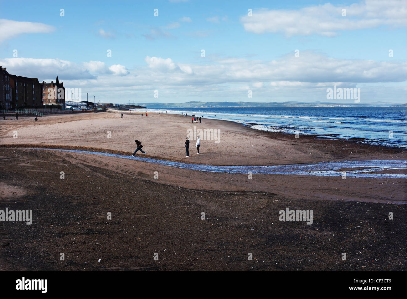 Ein junger Mann springt über einen Kanal Wasser am Strand von Portobello. Stockfoto