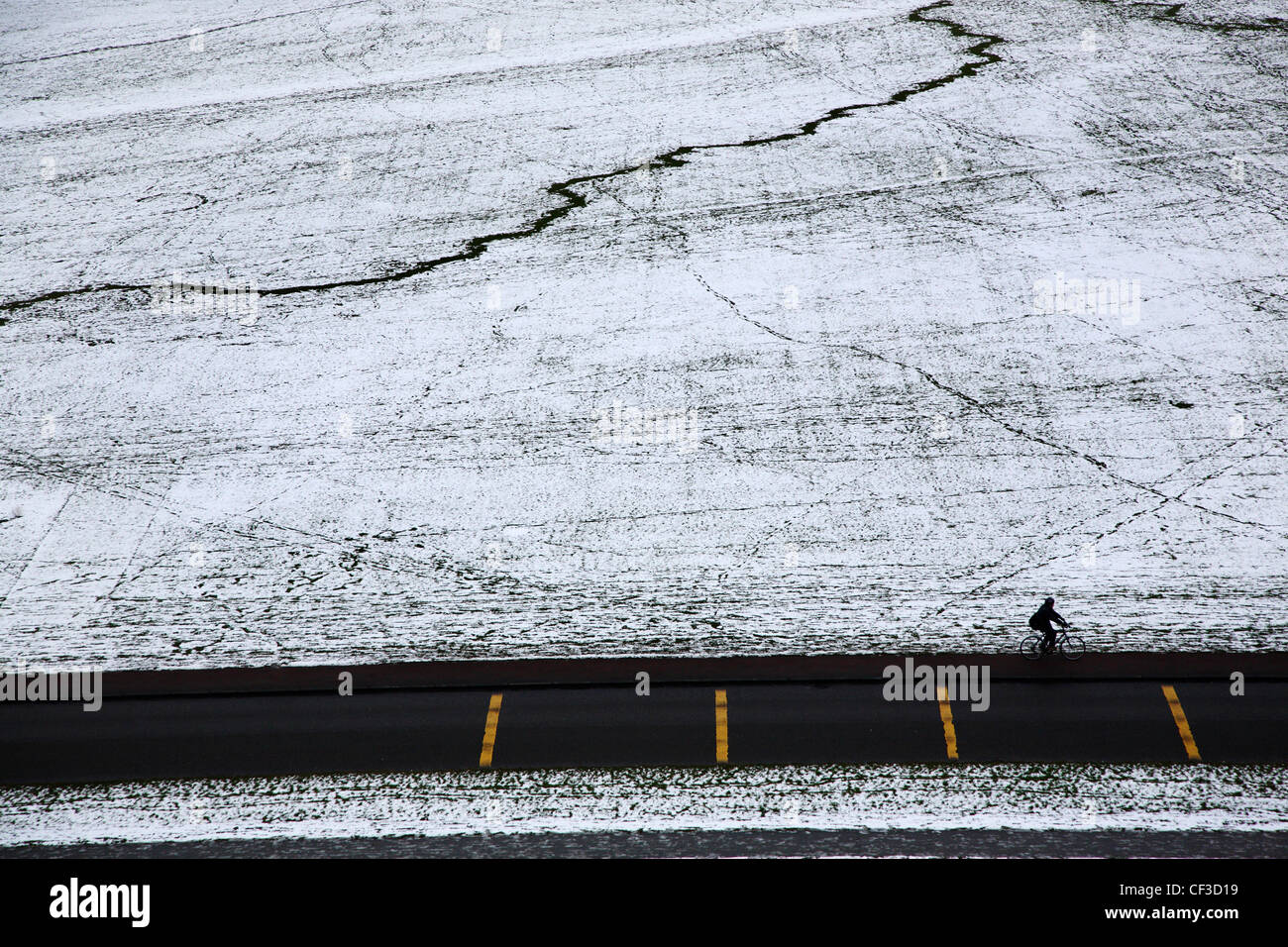 Silhouette eines Radfahrers Queens Drive entlang reiten, obwohl die schneebedeckten Gelände des Holyrood Park. Stockfoto