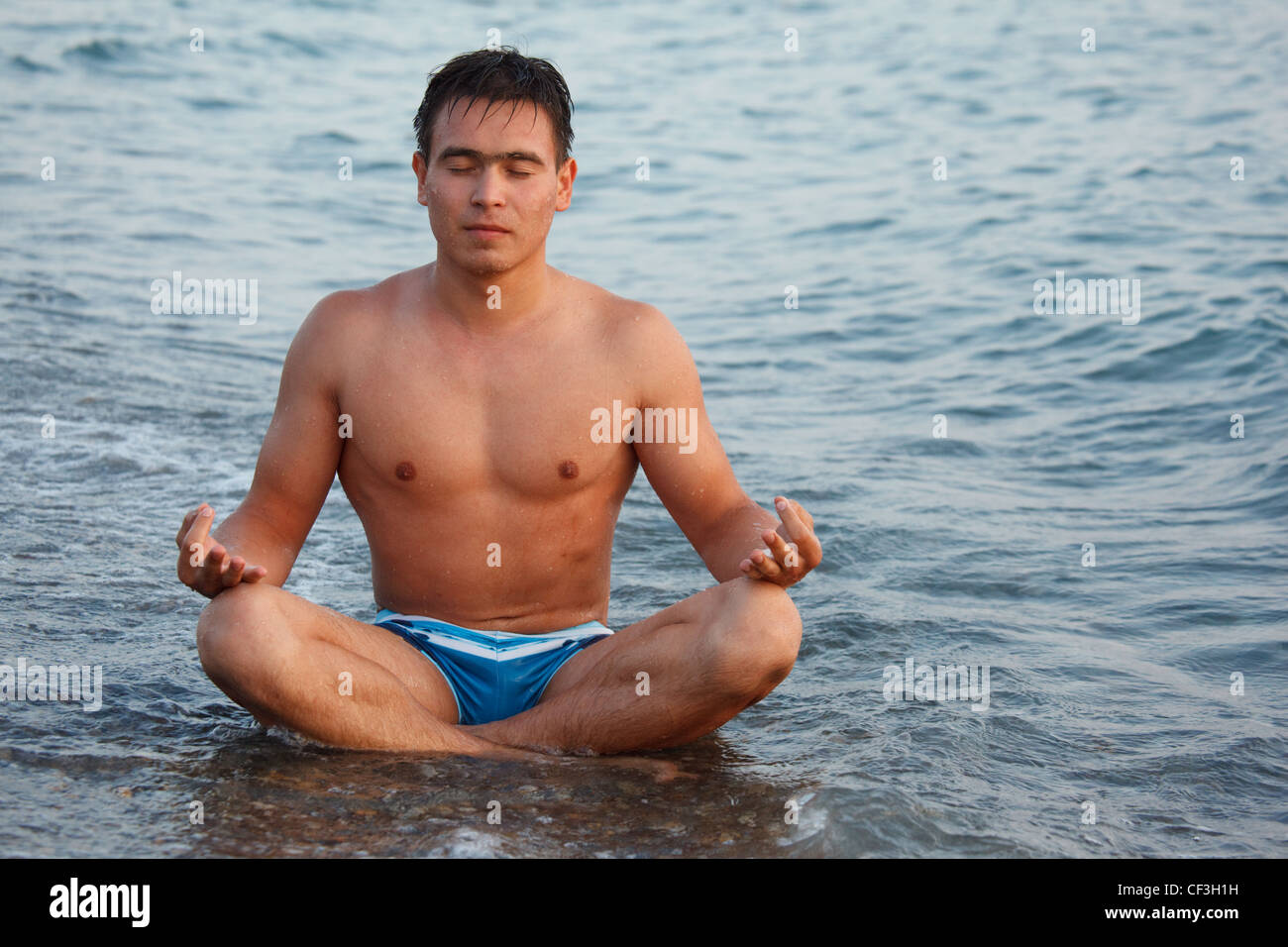 Junger Mann am Strand sitzen am Rand des Wassers zu meditieren. Stockfoto