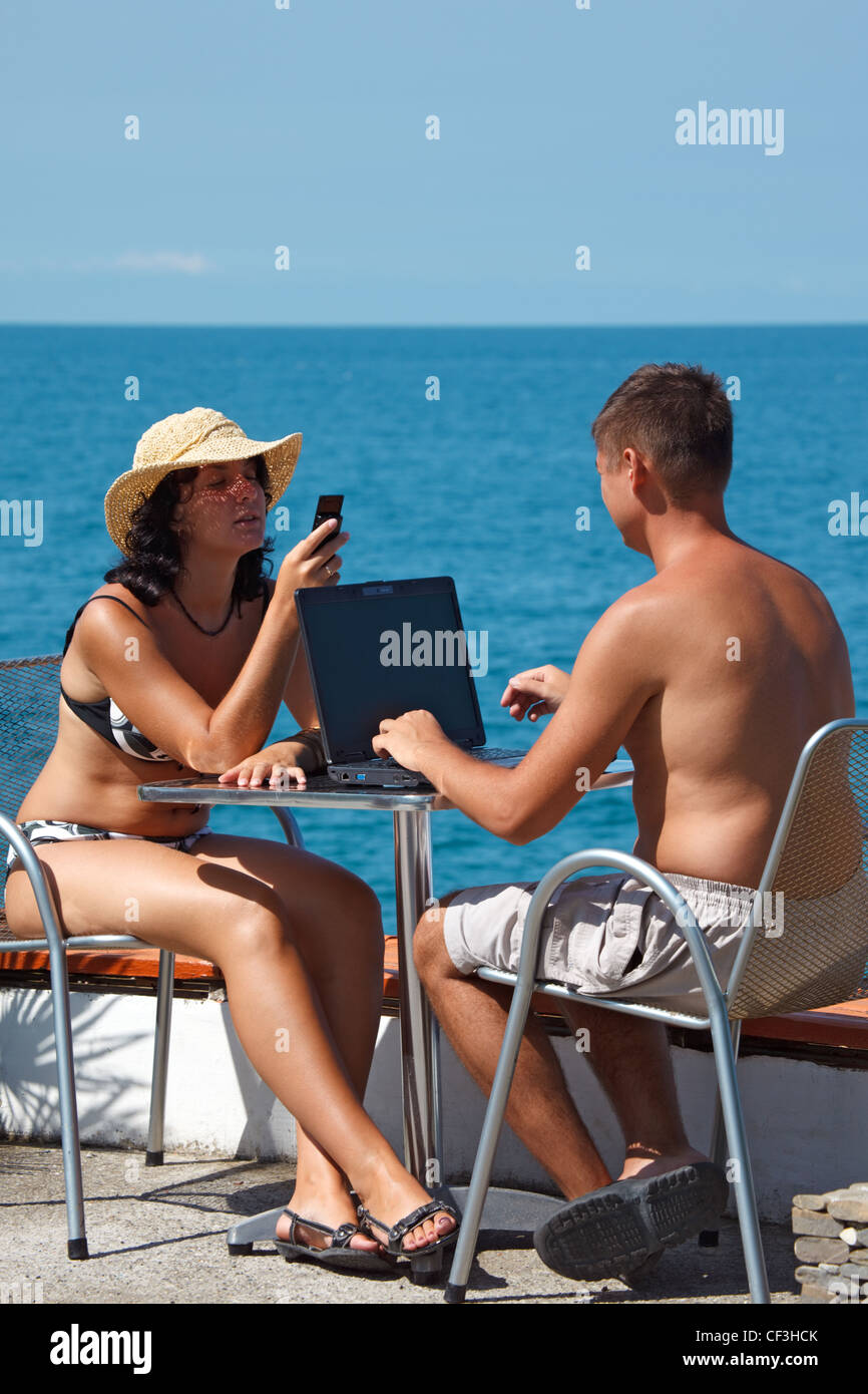 Mann und Frau sitzen am Tisch unter freiem Himmel auf Grund des Meeres. Mann arbeitet für Laptop. Hochformat. Stockfoto