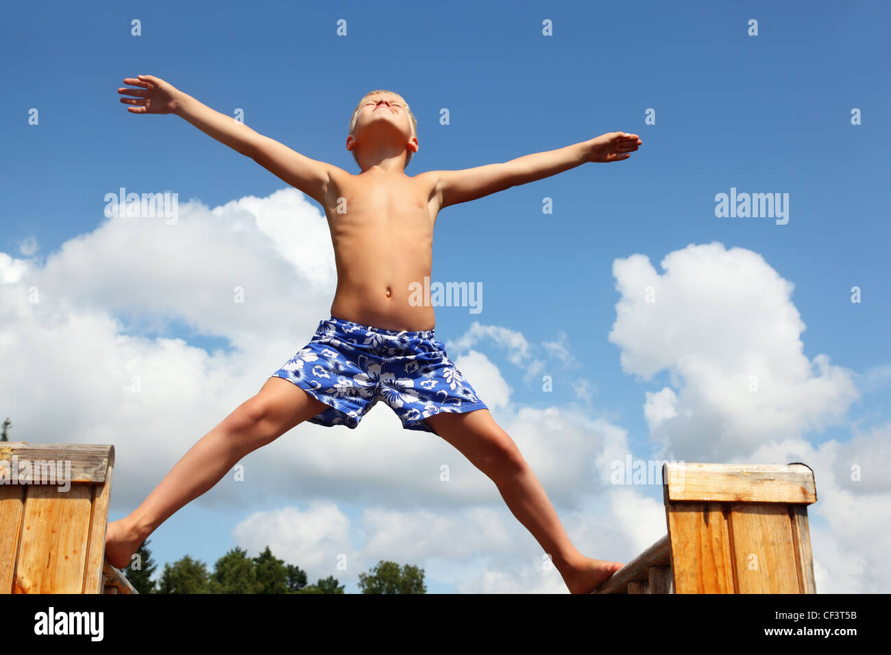 Junge in kurzen Hosen auf Bretter gegen Wolken, Pflanzen Hände und Beine in den Parteien stehend Stockfoto