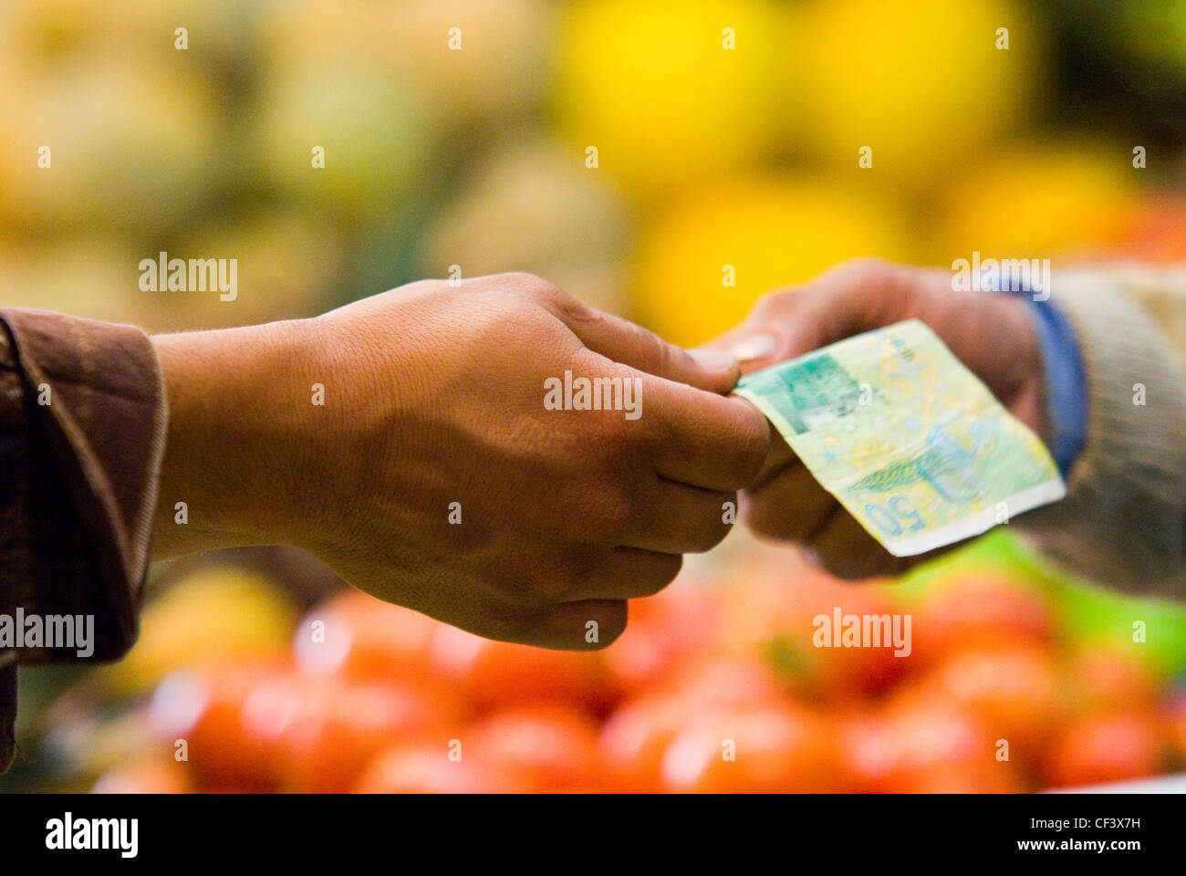 Geld wechselt vor dem Hintergrund von Obst und Gemüse in einer Markthalle in Marrakesch. Stockfoto
