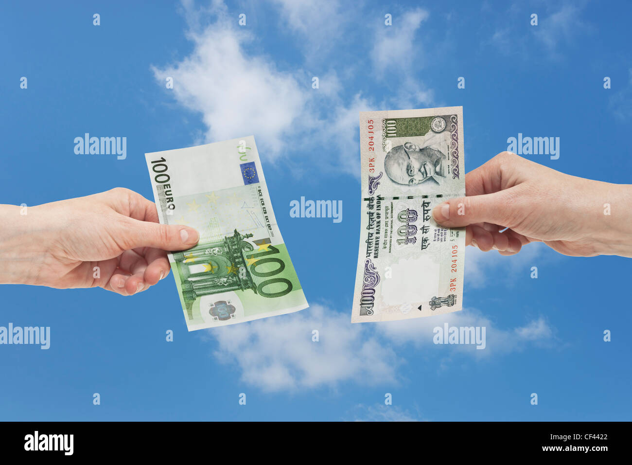 Eine indische 100 Rupie Rechnung ist in der Hand gehalten. Auf der anderen Seite ist ein 100 Euro-Schein in der Hand, Hintergrund Himmel gehalten. Stockfoto