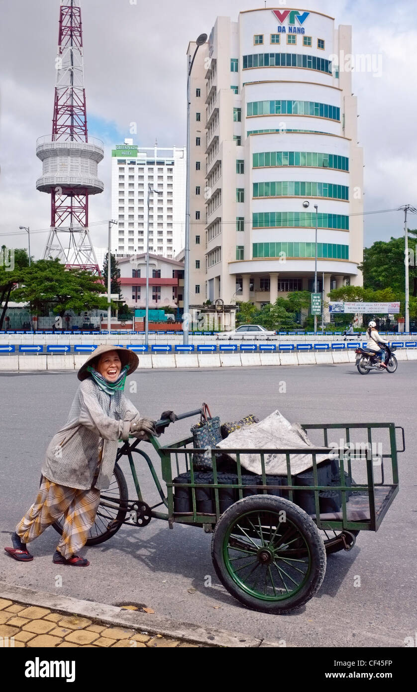 Lächelnde Frau Kohle Straßenhändler, ihre Lieferung Dreirad Fahrrad schieben, Bürogebäude, Da Nang, Vietnam, Südostasien Stockfoto