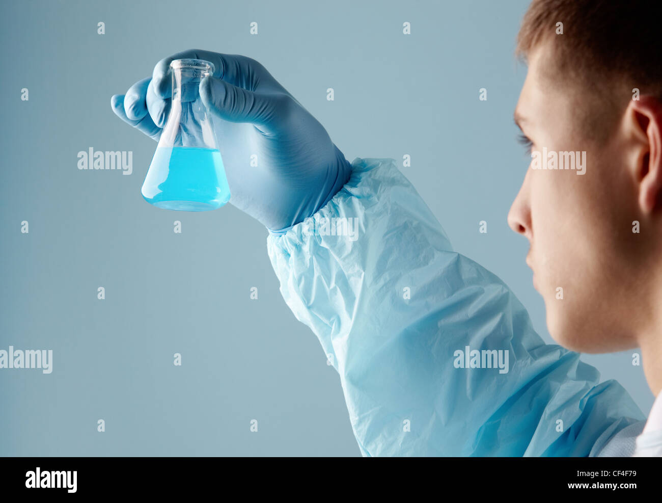 Männliche Chemiker hält einen kleinen Becher blaue Flüssigkeit gefüllt Stockfoto