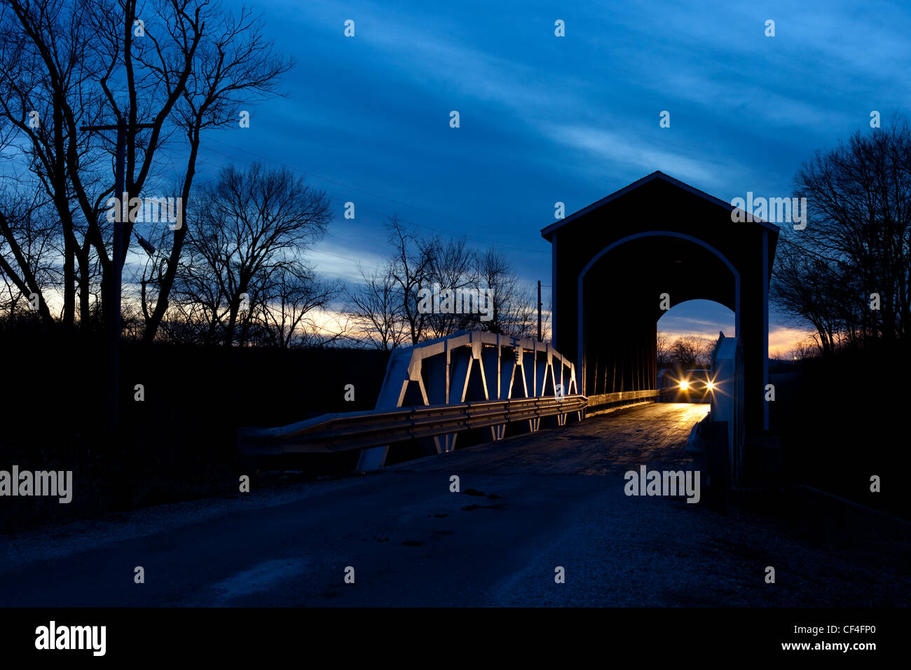 Ein Auto kreuzt eine überdachte Brücke im ländlichen Illinois kurz nach Sonnenuntergang an einem Wintertag. Stockfoto