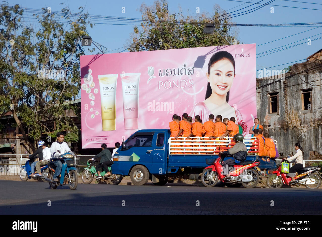 Eine Gruppe von buddhistischen Mönchen in einem Lastwagen vorbei an einem Teich Plakat Schild auf einer Stadtstraße in Pakse, Laos Reiten. Stockfoto