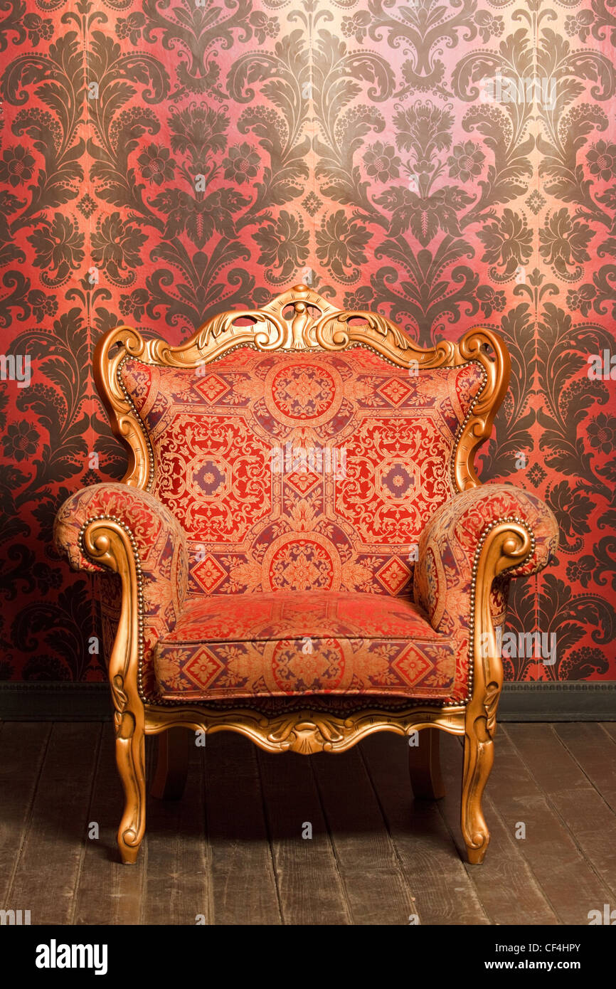 Vintage rot-gelb-Sessel mit goldenen Akzenten, die neben der Wand stand. Holzboden Stockfoto
