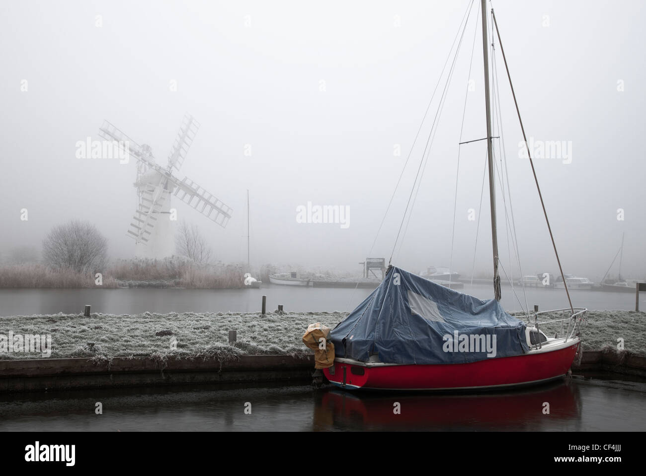 Thurne Windmühle steht im Nebel, während ein rotes Boot vor in den Vordergrund in Norfolk Anker. Stockfoto