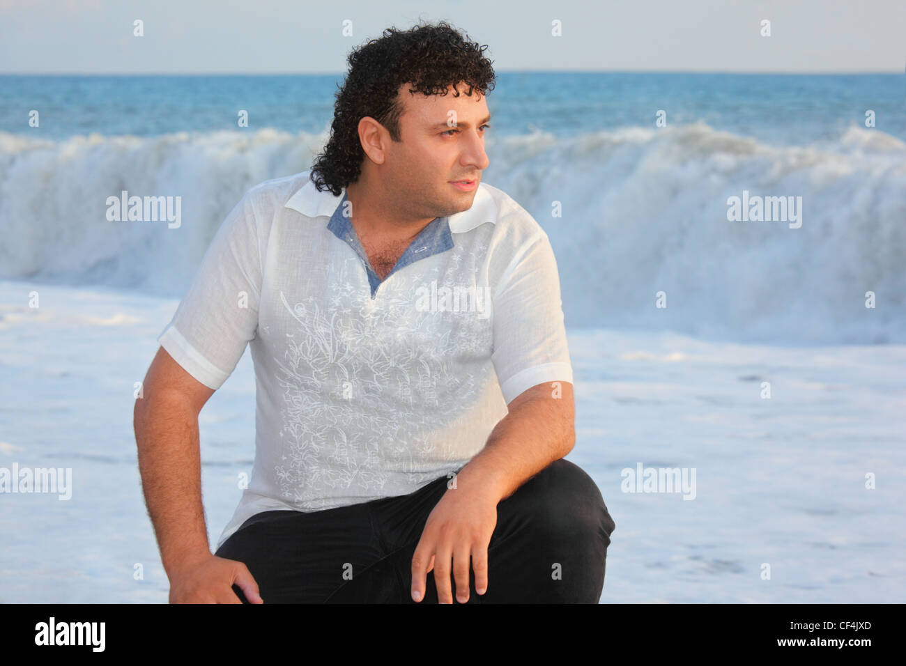 ein Mann sitzt in der Nähe von Wasser am Meer. Welle in unscharf Stockfoto