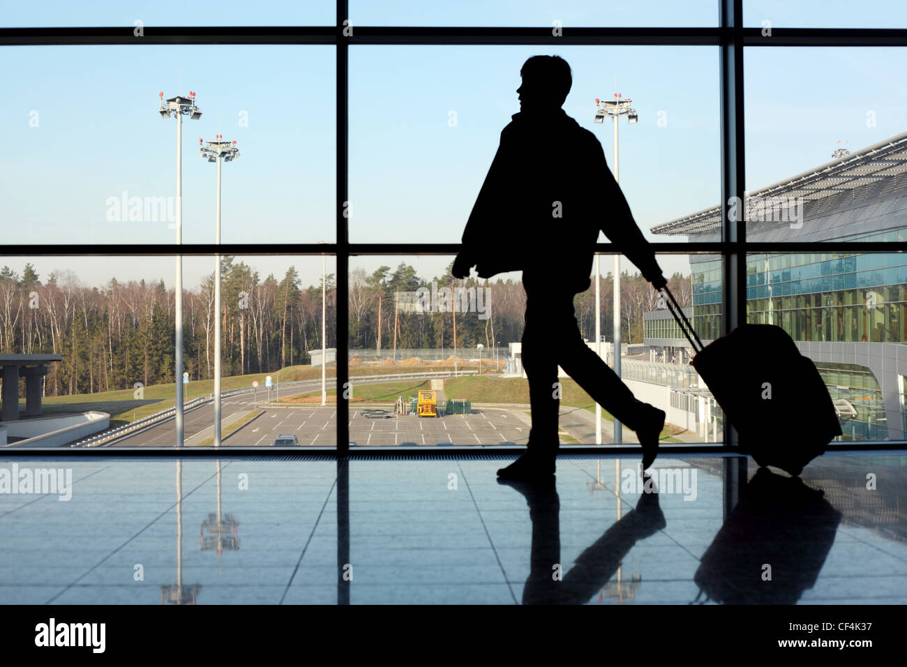 Silhouette des Mannes mit Gepäck zu Fuß links neben Fenster im Flughafen Fokus auf Straße Stockfoto