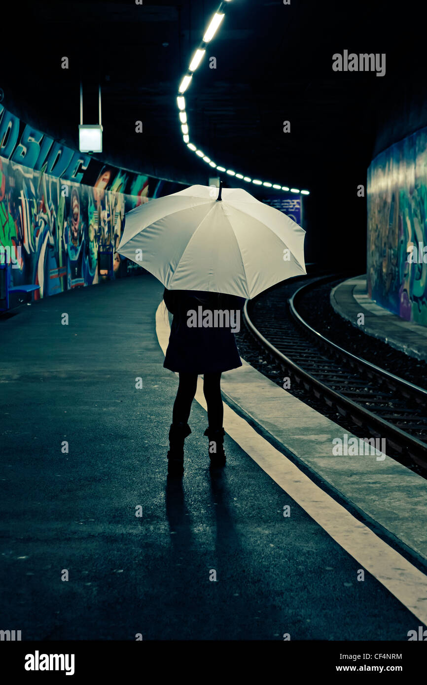Mädchen mit Regenschirm steht auf einer Plattform zu einer u-Bahnstation mit Graffiti und wartet. Stockfoto