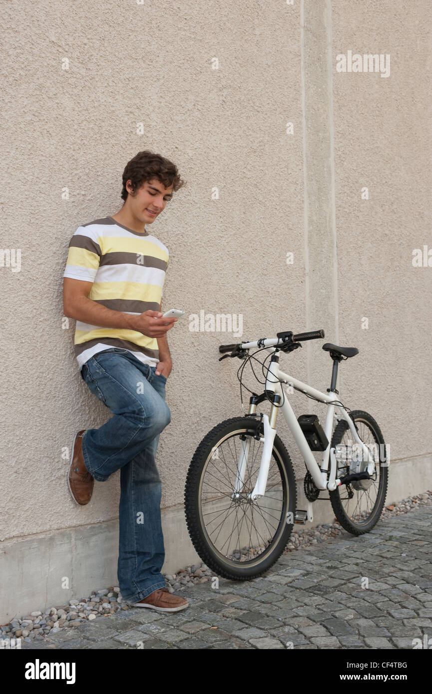 Deutschland, Bayern, junger Mann mit Handy stehend mit dem Fahrrad, Lächeln Stockfoto