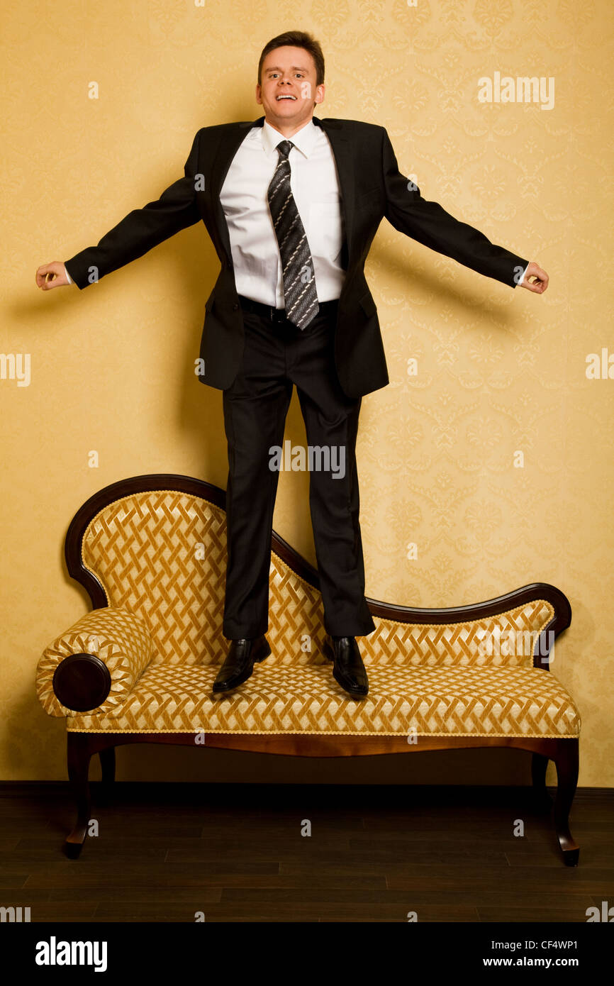 fröhliche Geschäftsmann im Anzug springen auf Sofa im Raum Stockfoto