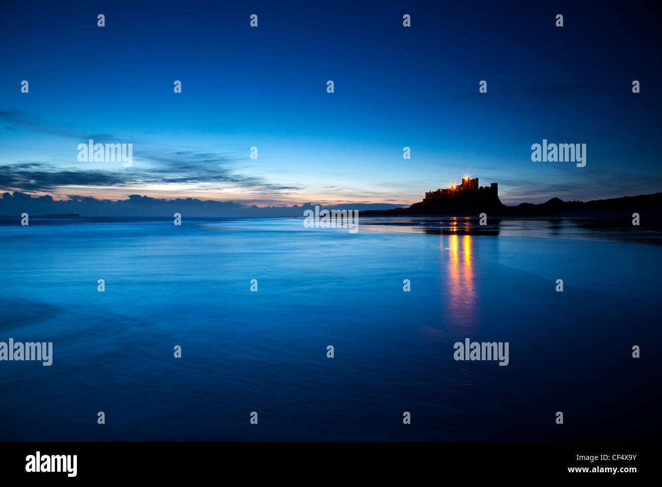 Lichter von Bamburgh Castle reflektierenden in der Ebbe kurz vor der Morgendämmerung. Stockfoto