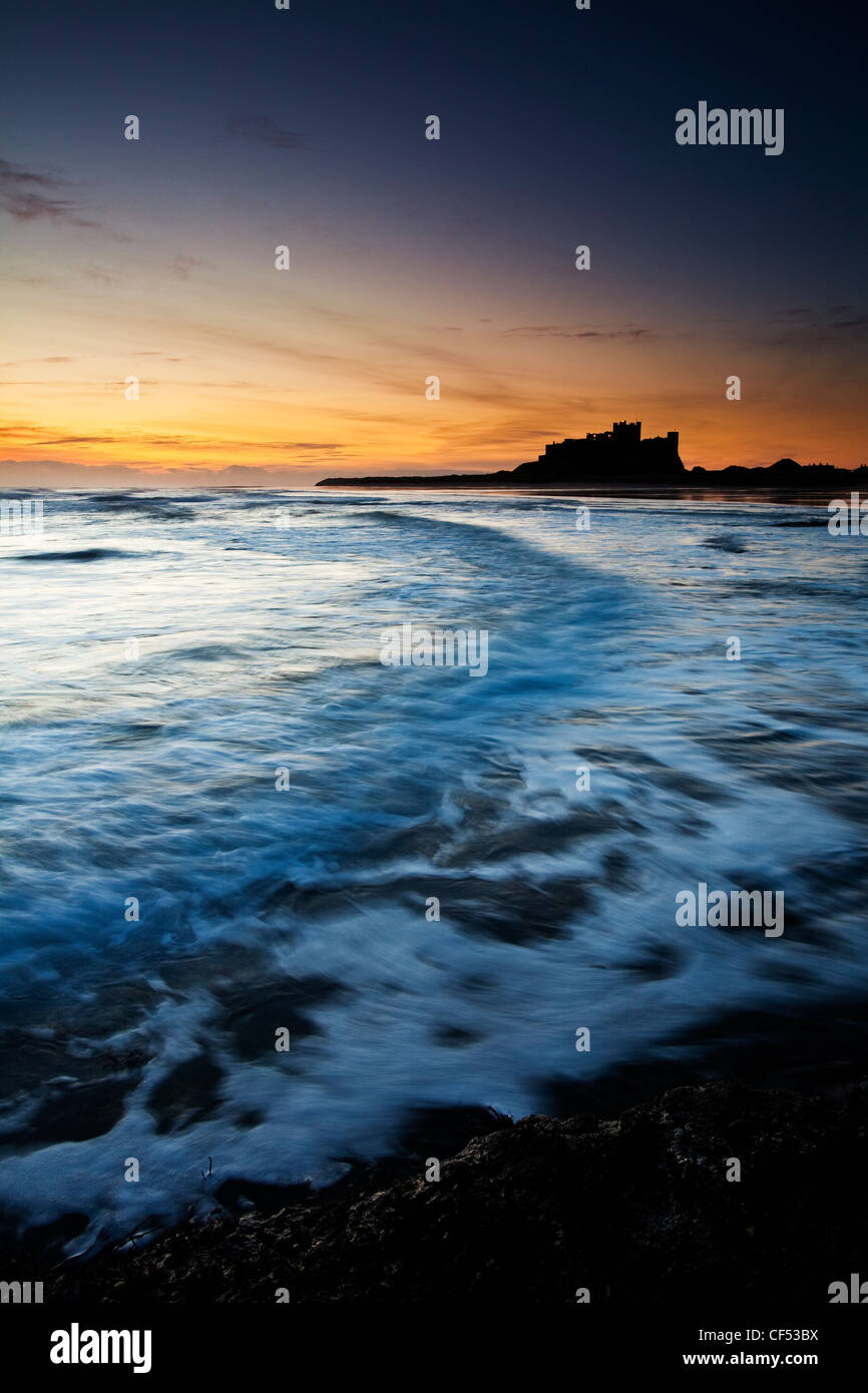Wellen auf den Strand von Bamburgh Castle in der Morgendämmerung. Stockfoto