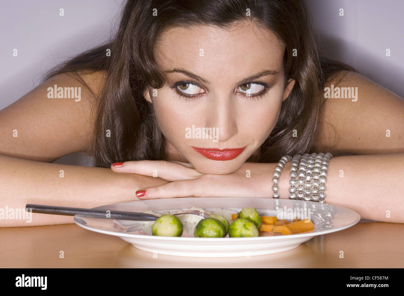 Weibliche brünette Haare tragen braune smokey eyes Make-up am Tisch gelehnt auf Tisch Kinn auf die Hände ruhen verschränkten Armen, Stockfoto