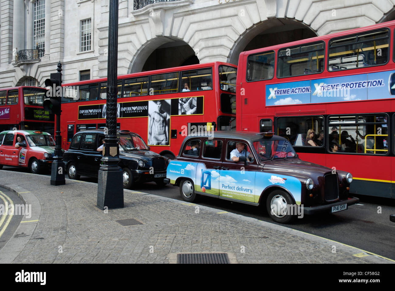 Drei traditionelle Londoner Taxis und drei roten Londoner Busse mit eleganten viktorianischen Gebäuden im Hintergrund. Stockfoto