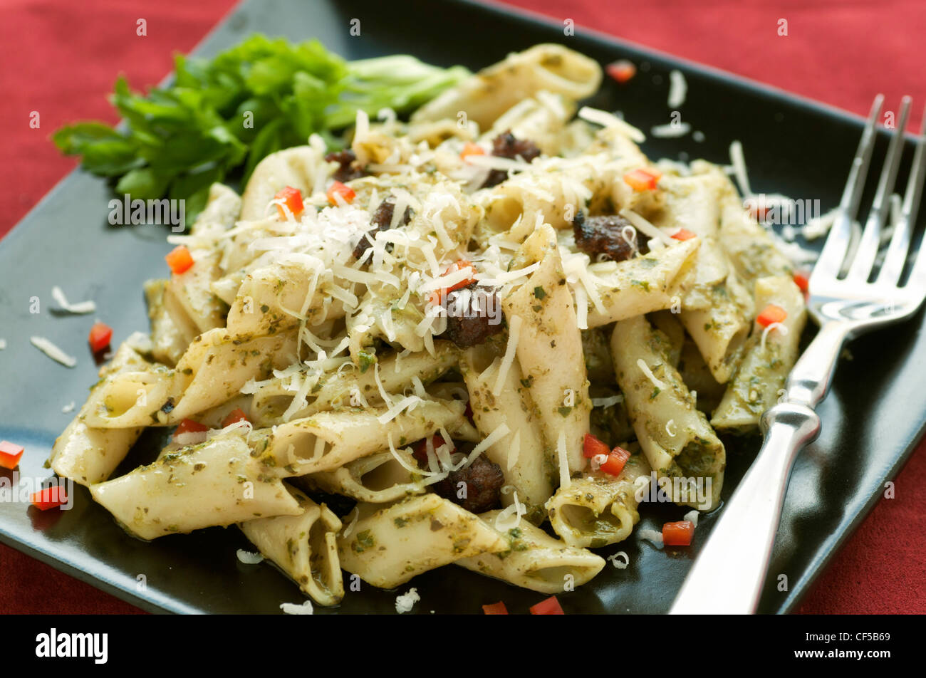 Penne-Nudeln mit Pesto, Frischwurst und gewürfelte Paprika auf schwarze Platte und rot Tischset Stockfoto